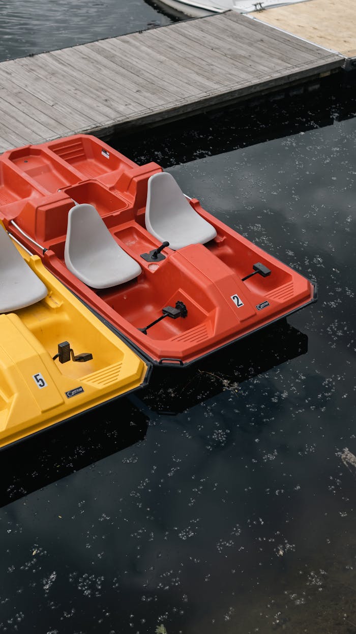 A vibrant scene of red and yellow paddle boats docked at a jetty on a serene pond.